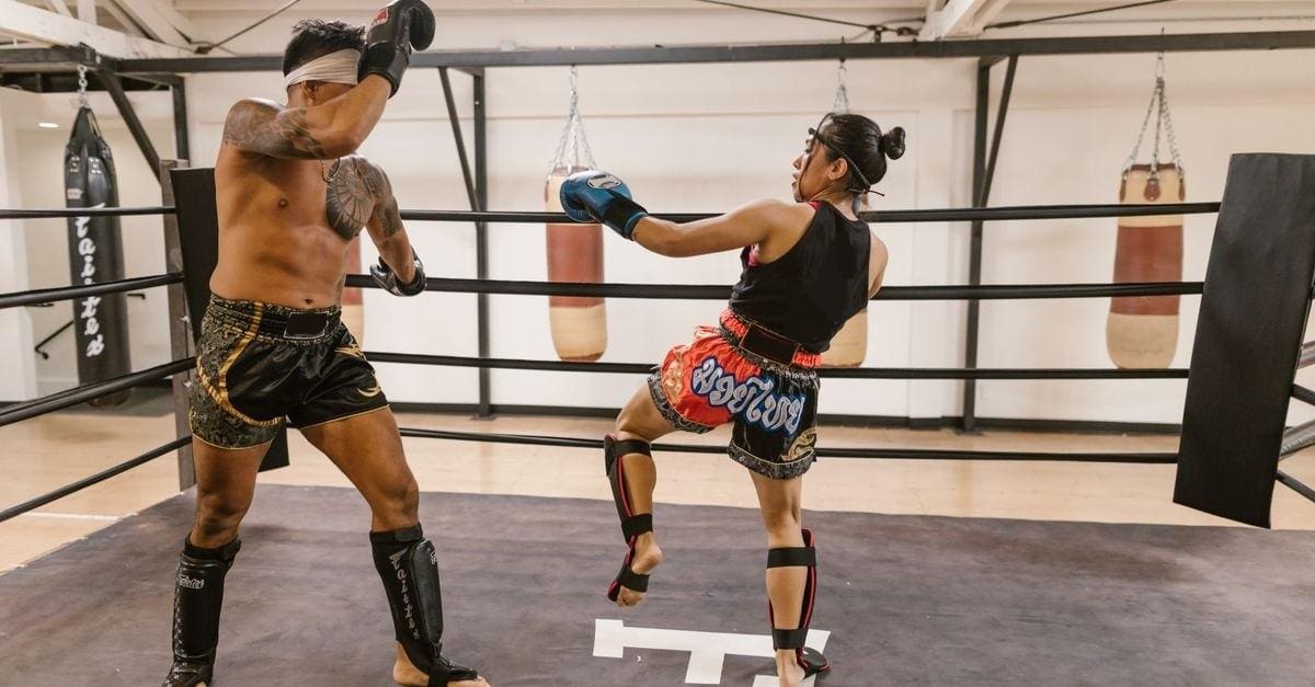 Two fighters sparring inside a boxing ring, practicing Muay Thai striking techniques and defensive head movement.