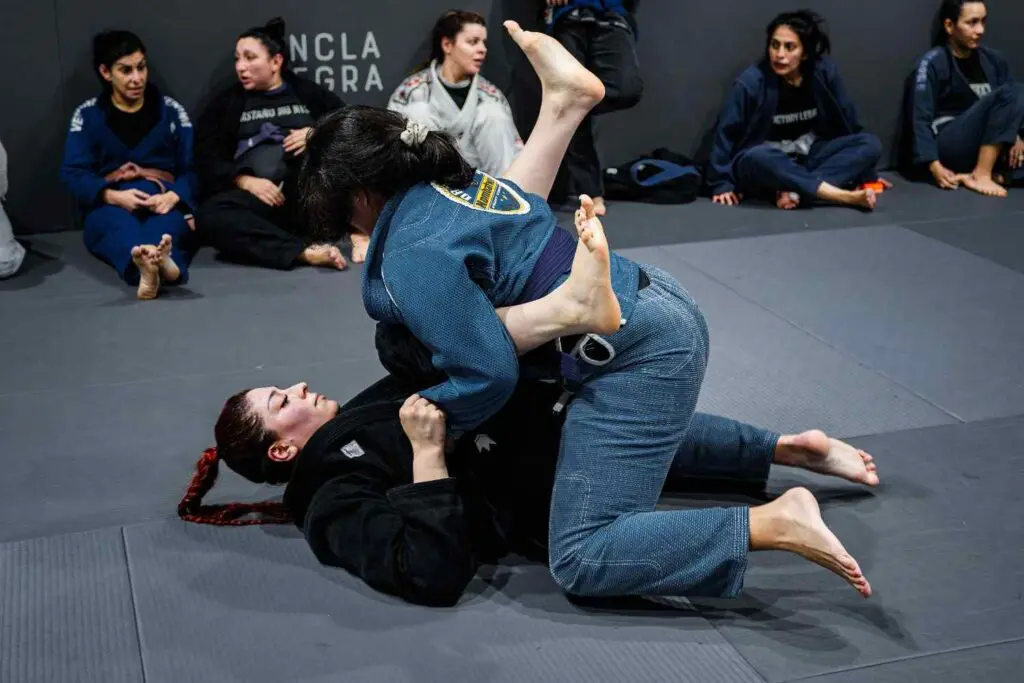 A female student maintaining mount and chest-to-chest top control against a partner during live mat rolling, utilizing adult Brazilian Jiu Jitsu positional hierarchy.