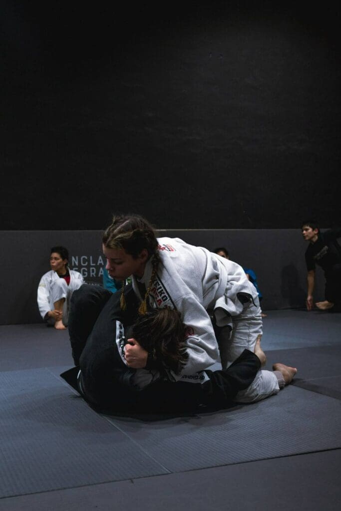 A female athlete holding top control in open guard against an opponent on the mat, refining adult Brazilian Jiu Jitsu positional hierarchy.