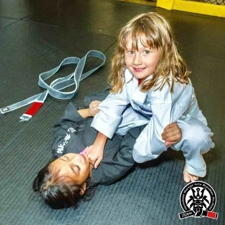 A young girl smiling while practicing a mount control drill on a partner during kids Jiu-Jitsu practice, how to improve faster in martial arts classes