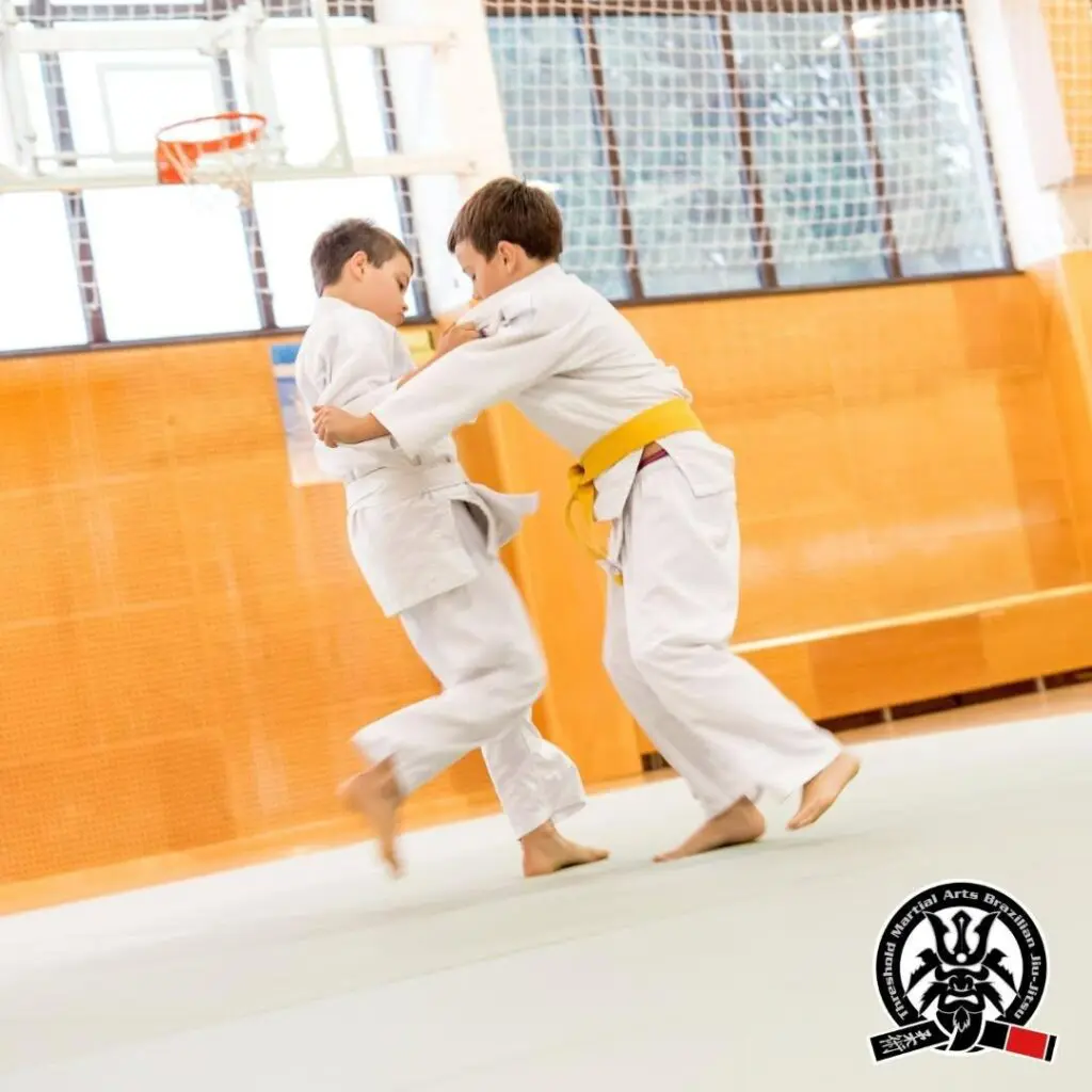 Two young boys practicing grip fighting and judo throws inside a sports gymnasium, demonstrating how to improve faster in martial arts classes